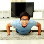 Portrait of a smiling  young man doing push ups in the living room at home