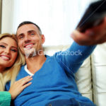 Cheerful young couple sitting on the sofa and watching TV