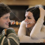 Young romantic couple sitting on sofa in front of fireplace at h