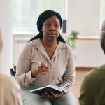 Young confident black woman with notebook and pen consulting patients